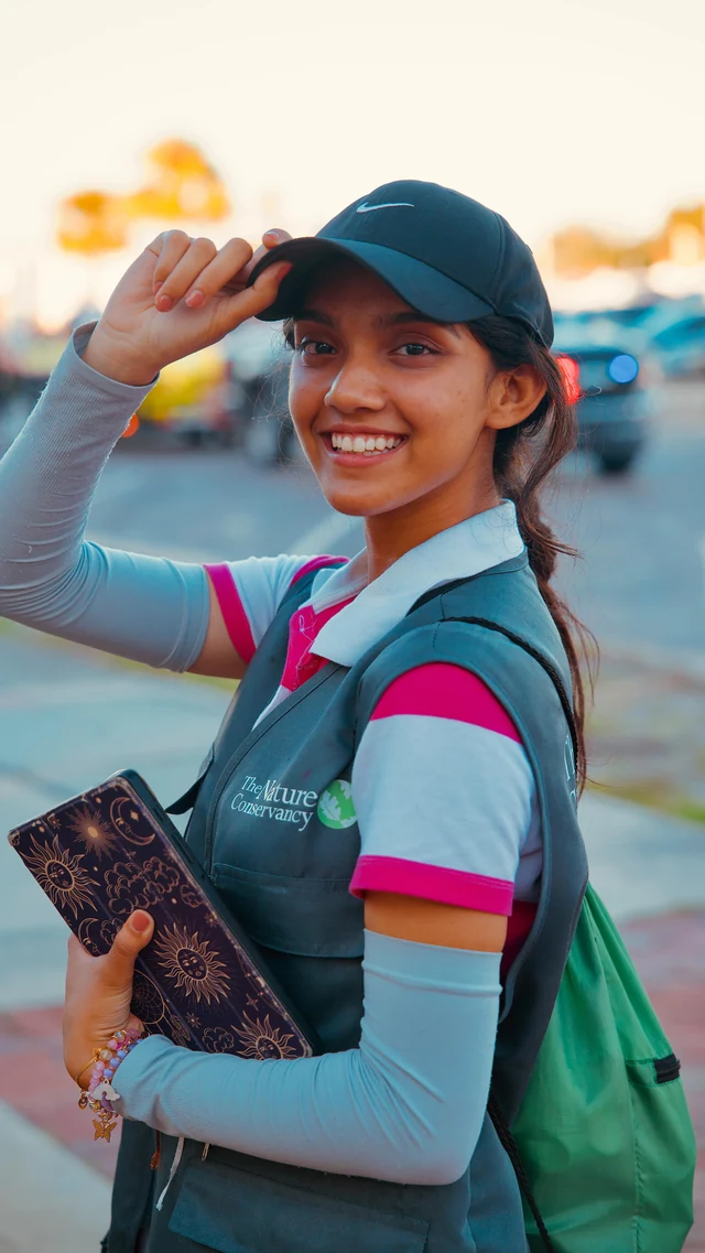 A reel cover of a smiling woman in a navy cap and conservation vest holding a patterned journal