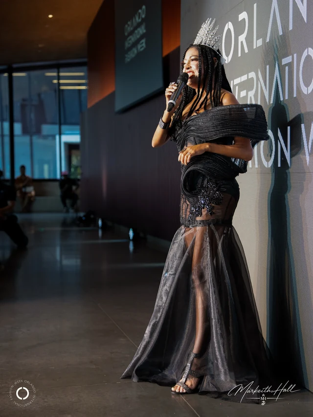 Zaneta Bailey wearing a crown and black gown while speaking at an event