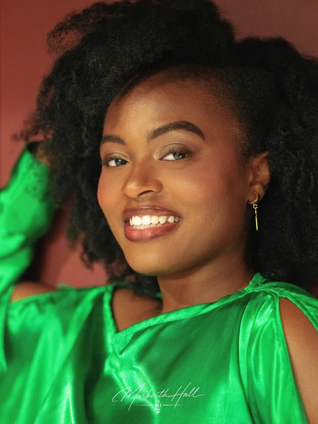 A smiling woman in an emerald green dress against a burgundy backdrop