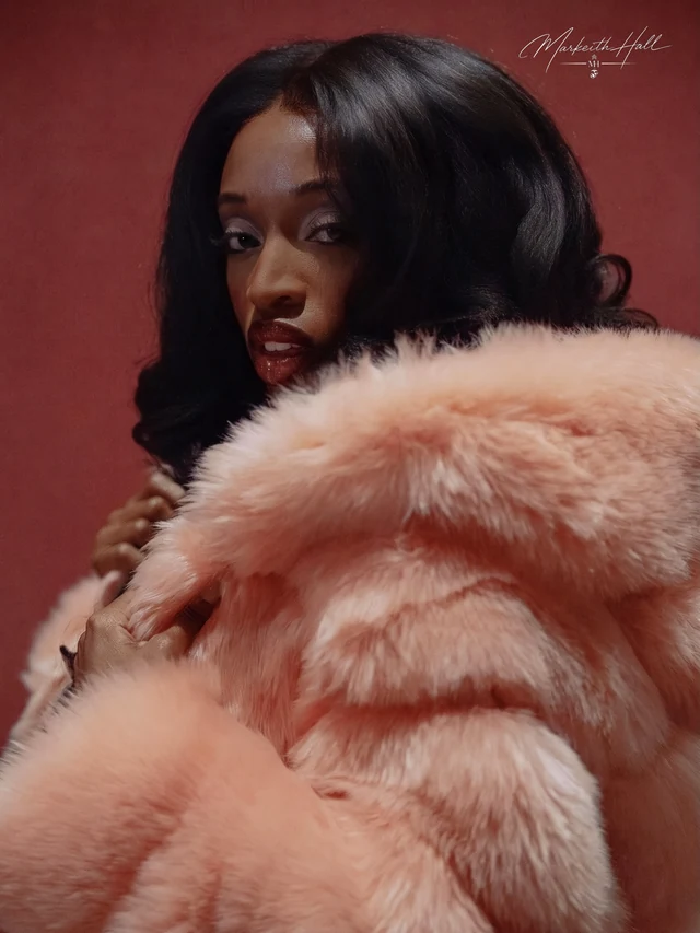 A woman looking over her shoulder in a pink fur coat against a burgundy backdrop