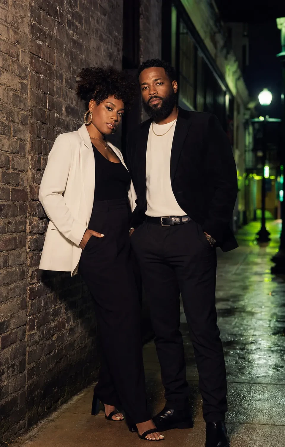 A couple in evening clothes posing together beside a brick wall outdoors