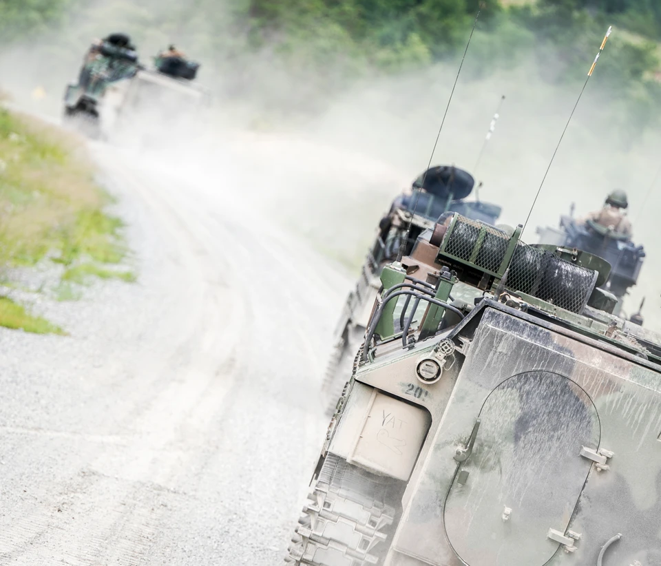 Amphibious assault vehicles move along a dusty road toward a training area