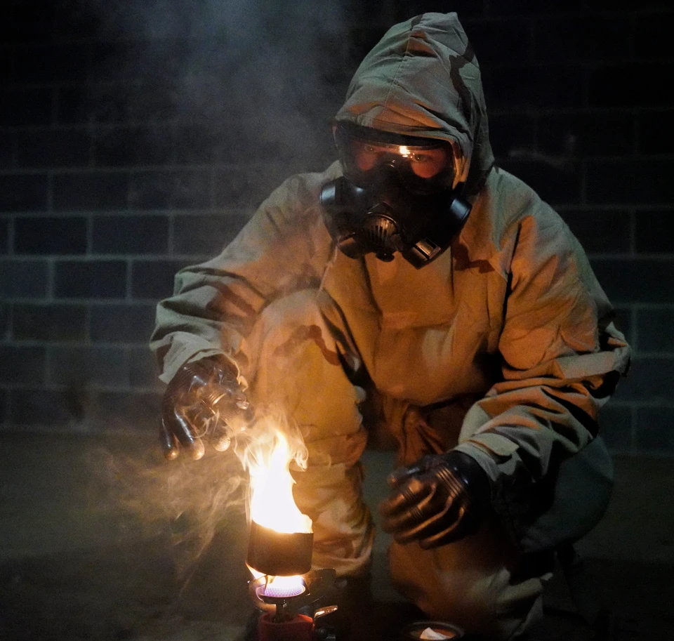 A Marine in protective equipment prepares CS gas as a flame illuminates his gloves and goggles