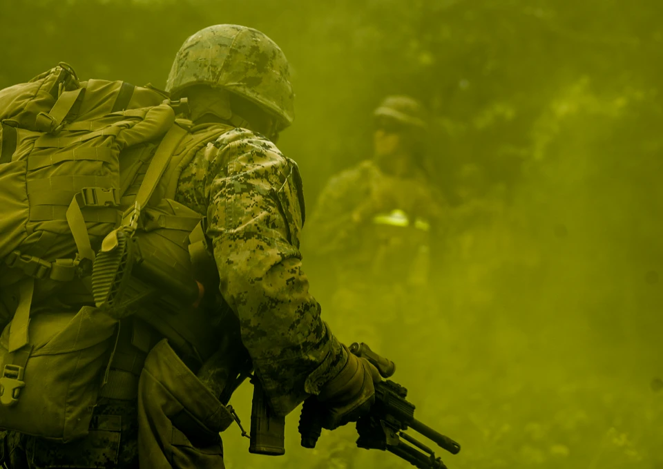 A Marine in the foreground faces a teammate visible through layered yellow-green smoke during training