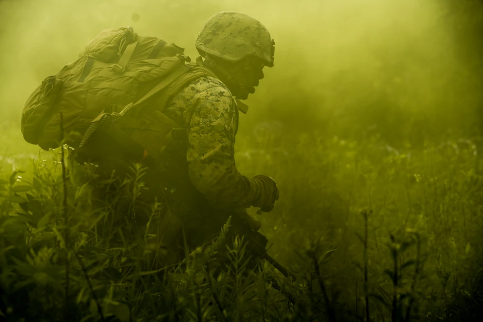 A Marine crouches amid yellow-green smoke during a field training drill