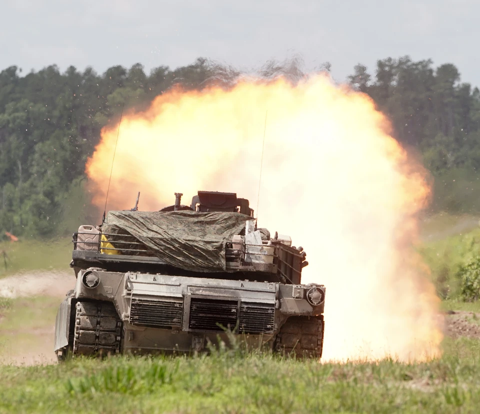 A tank seen from behind with a bright muzzle blast during live-fire training