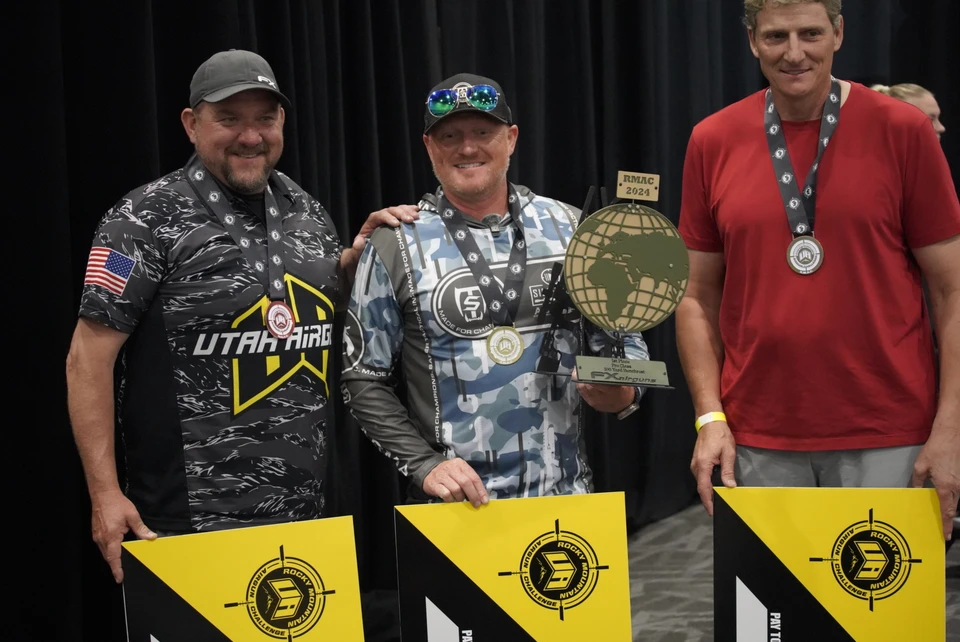 Three RMAC competitors stand together with medals, prize checks, and a trophy marked RMAC 2024