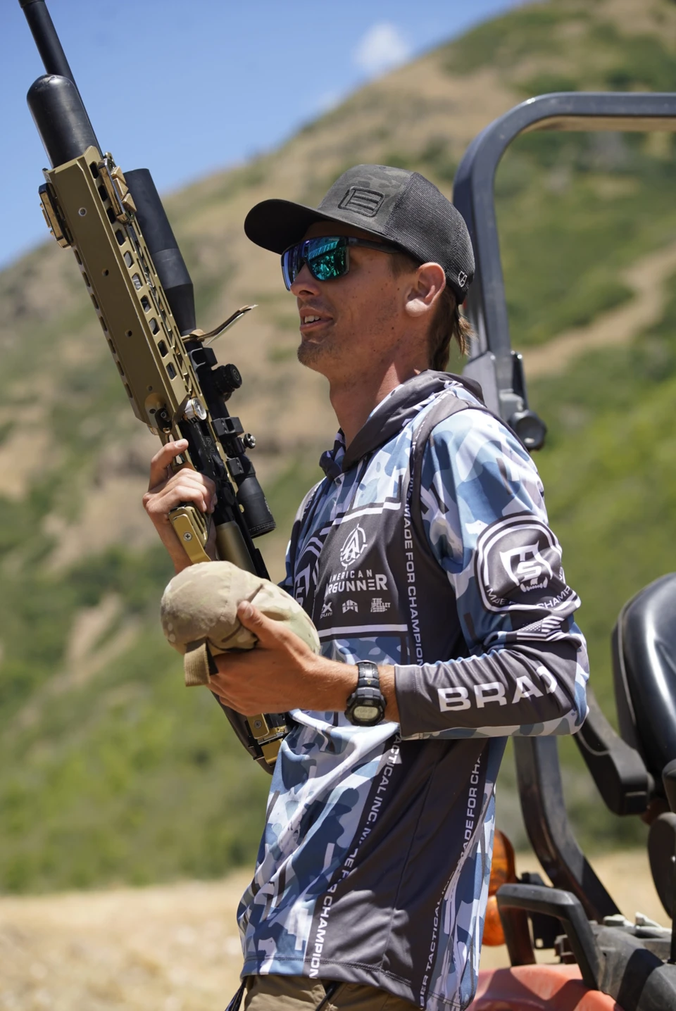 An RMAC competitor carries his air rifle beside a grassy hillside